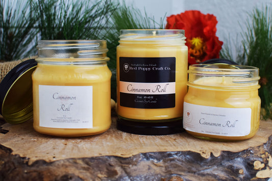Three jars of 'Cinnamon Roll' candles on a wooden surface with a floral background.