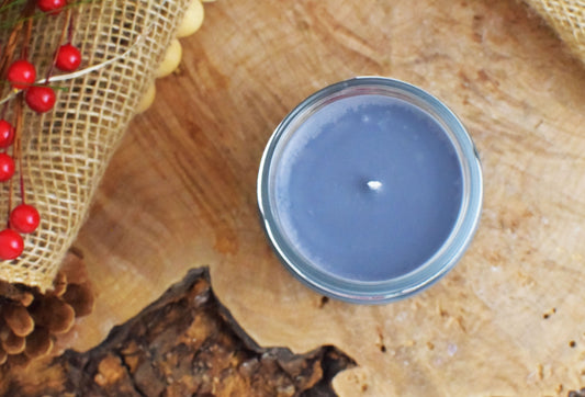gray candle in a glass jar on a wooden surface with red berries and burlap.