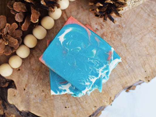 Two blue and white marbled soap bars on a wooden surface with pinecones and beads.