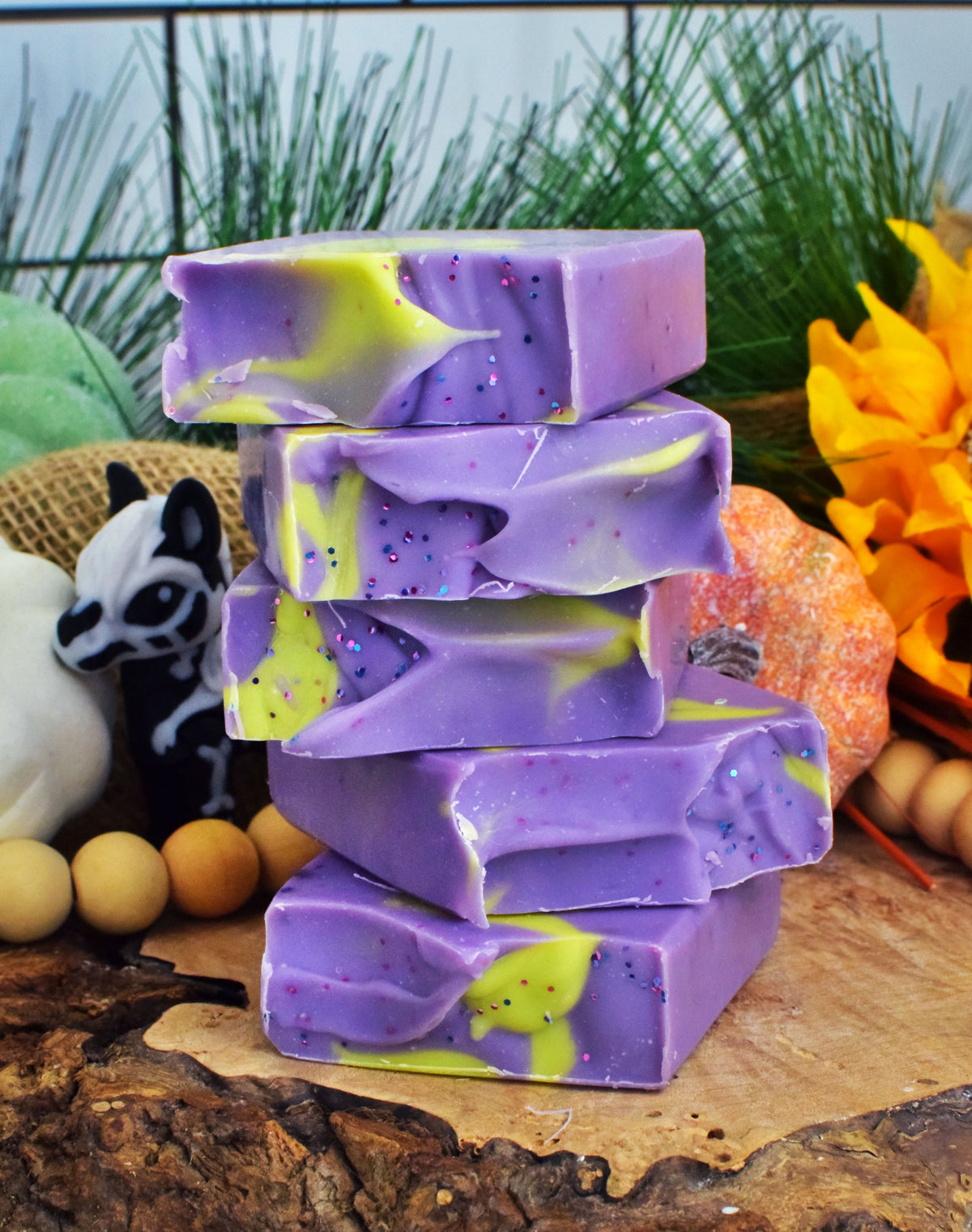 Stack of purple and green soap bars on a wooden surface with decorative items in the background.